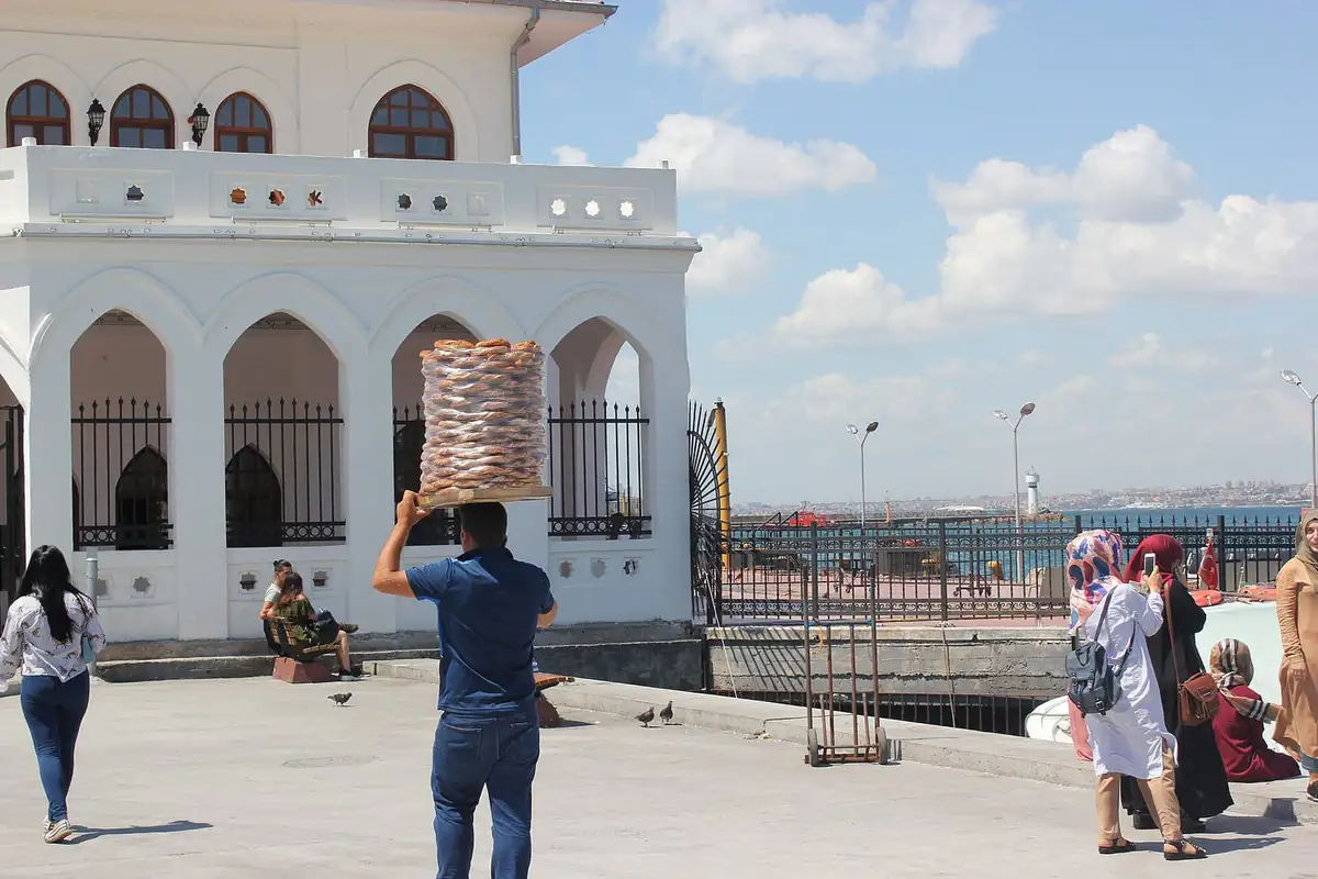 A street vendor balancing a tall tray of simit rings on his head by the waterfront