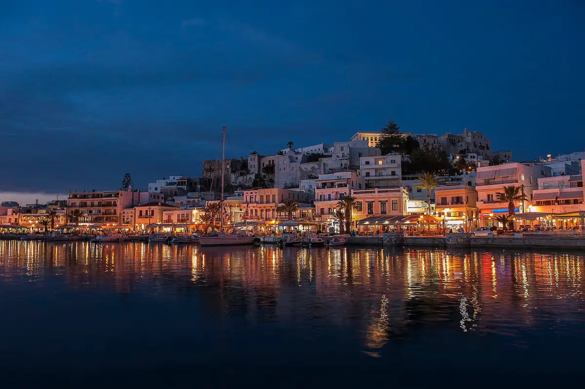 Naxos Town waterfront lit up at dusk, with lights reflected in the harbour and the kastro on the hill above