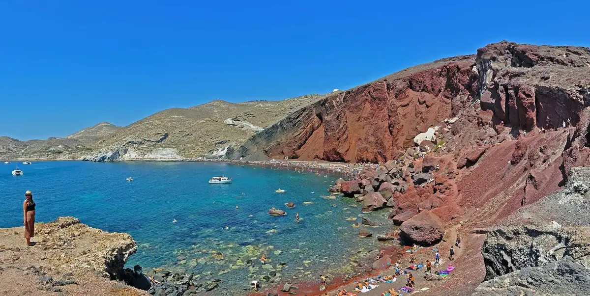 Red Beach on Santorini with red cliffs, swimmers and boats in a blue bay