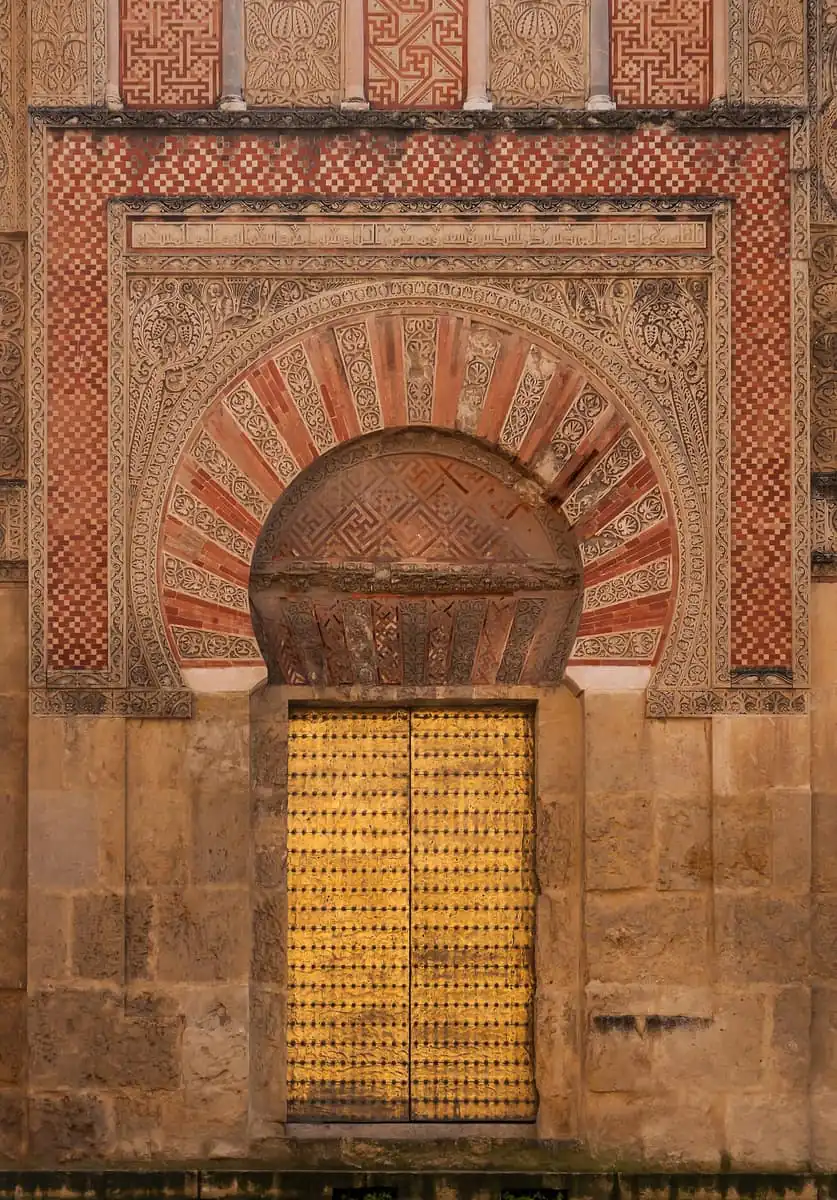 A carved horseshoe-arch doorway with golden doors on the outer wall of the Mezquita in Cordoba