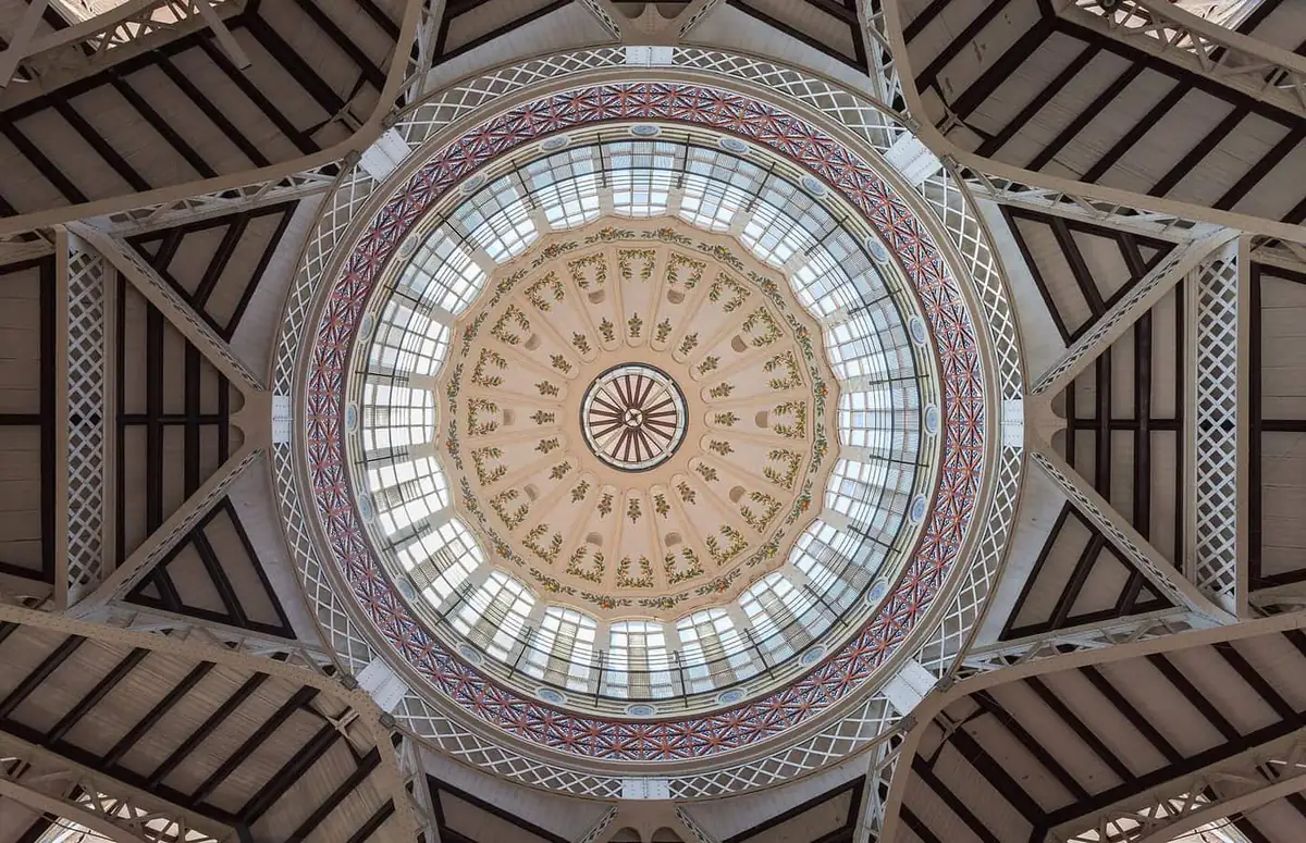 Looking up at the painted central dome of Mercado Central in Valencia, with iron trusses radiating from a glass lantern
