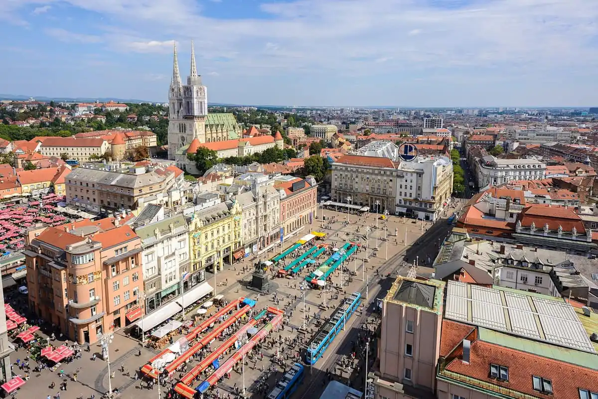 Aerial view over Ban Jelačić Square in Zagreb with the cathedral spires, the red parasols of Dolac market and a blue tram