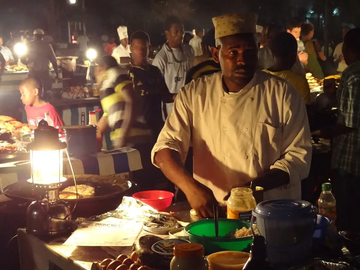 A cook preparing food at a lit stall in Forodhani Gardens night market in Stone Town