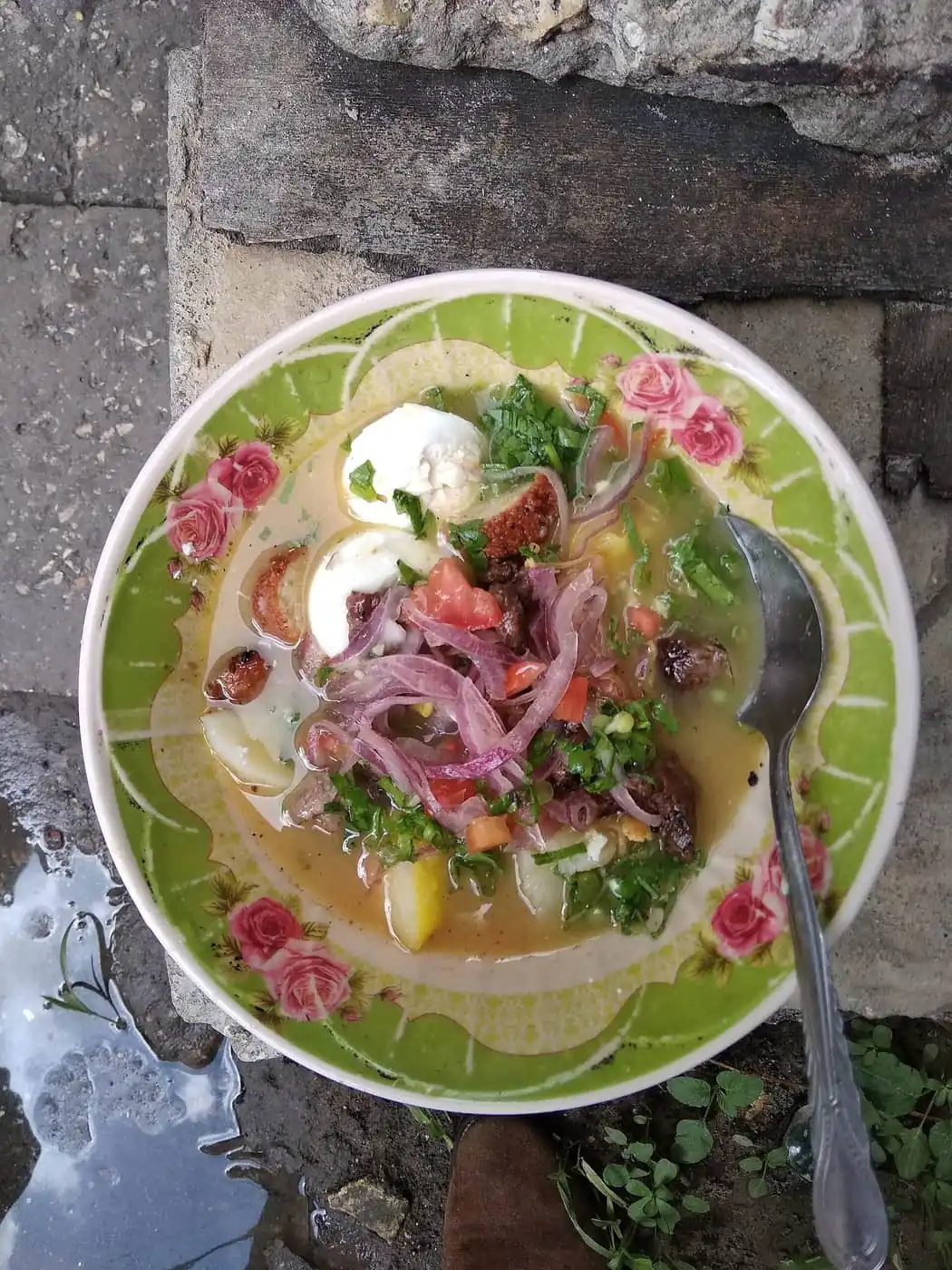A bowl of urojo topped with egg, red onion, tomato and herbs
