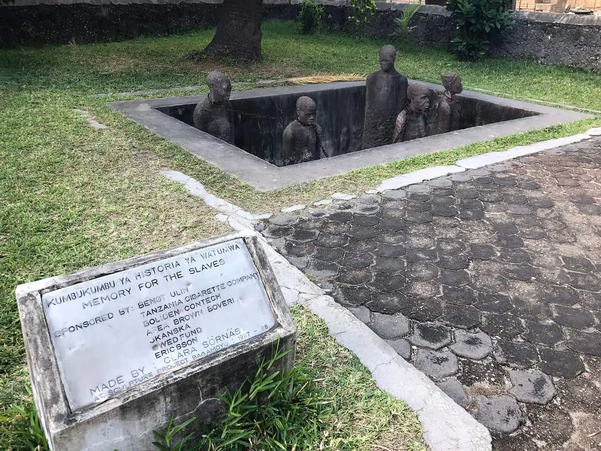 Chained statues standing in a pit at a memorial site with a plaque