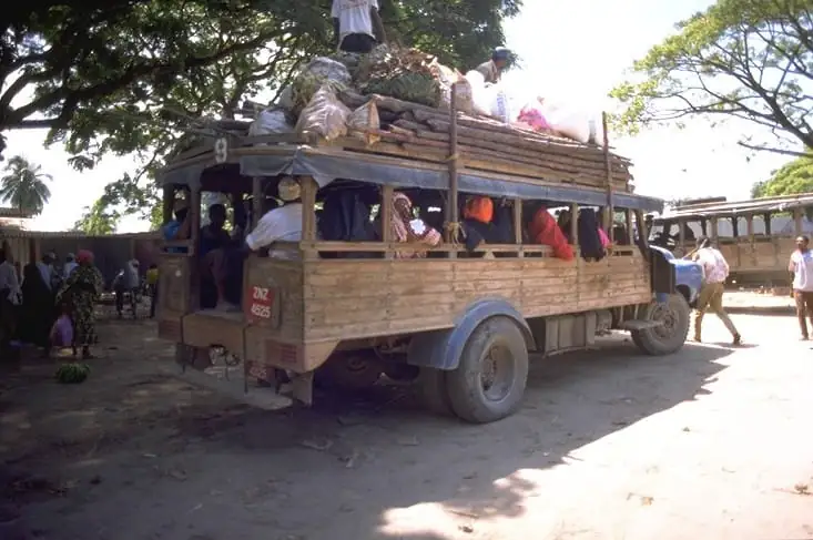 A wooden mabasi bus loaded with goods and passengers at a dusty stop